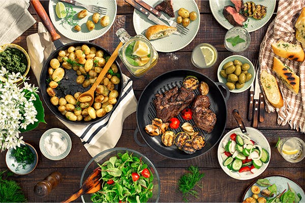 Dinner-table-with-meat-grill,-roast-new-potatoes,-vegetables,-salads,-sauces,-snacks-and-lemonade,-top-view